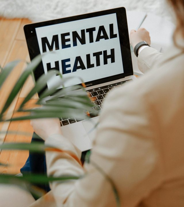 A woman focuses on mental health resources through her laptop in a home office setting.